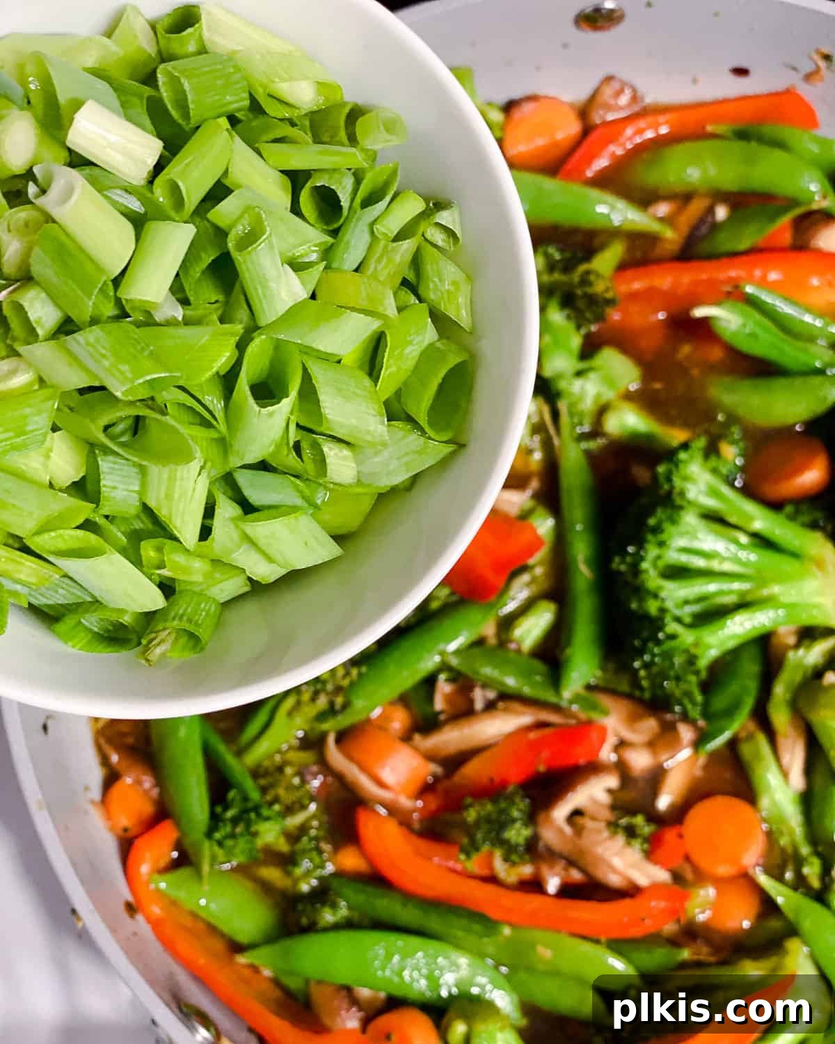Freshly chopped green onions being sprinkled over the completed stir-fry vegetables in the pan, adding a final touch of vibrant color and fresh flavor.