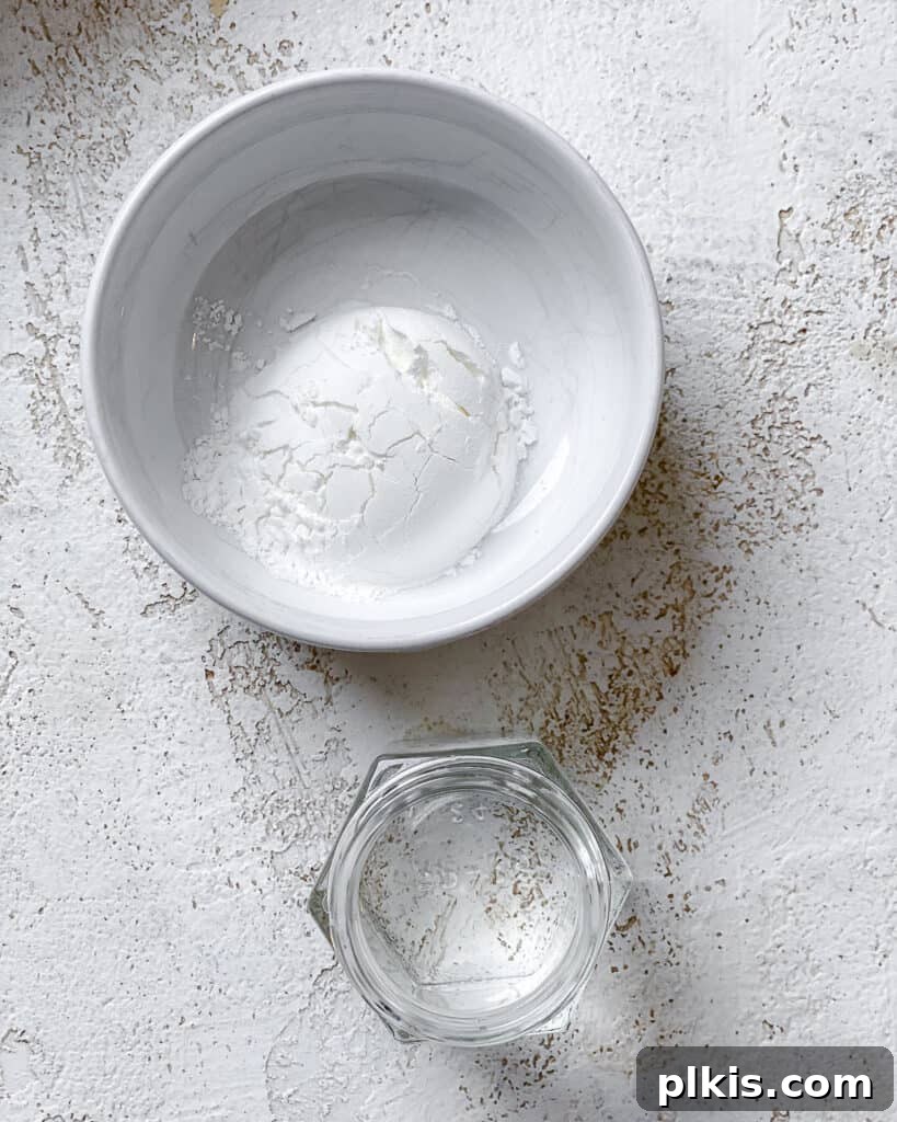 Individual bowls holding cornstarch and cold water, precisely measured for the stir-fry sauce.