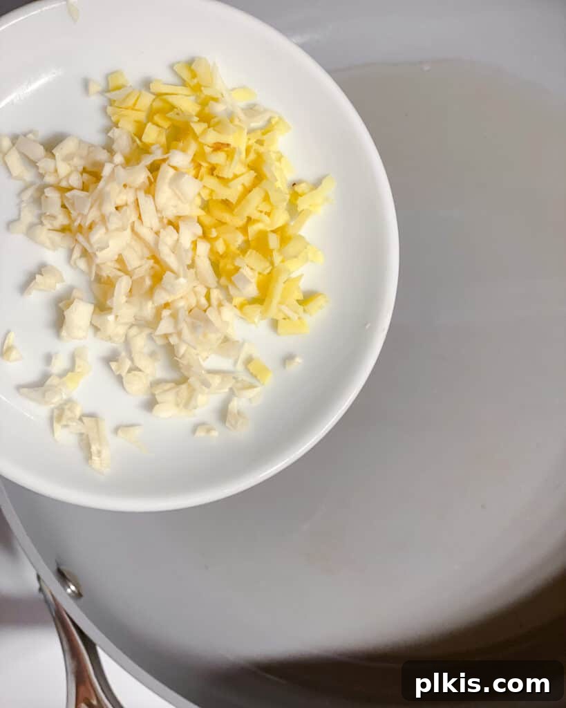 Minced garlic and ginger being added to a hot pan with oil, releasing their fragrant aromas as they begin to sauté.