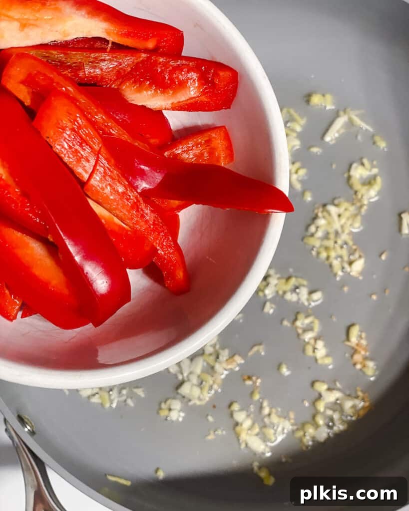 Sliced bell pepper being added to the hot pan, joining the aromatics to begin stir-frying.