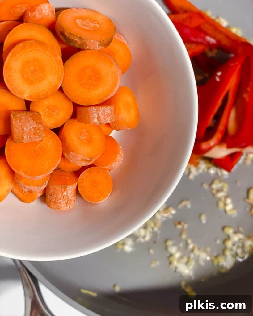 Sliced carrots being added to the pan, contributing to the colorful mix of stir-frying vegetables.