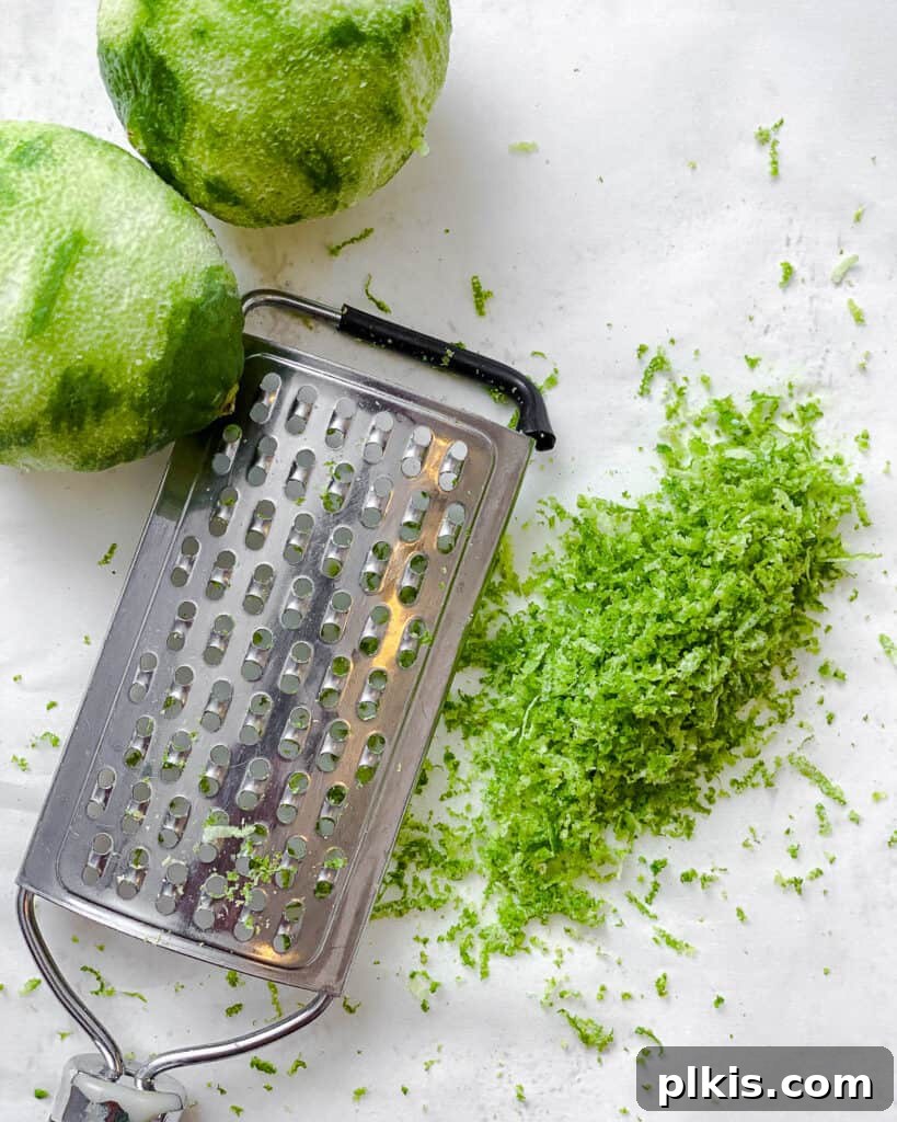 Make Your Own Tangy Chili Lime Dust 4 A hand using a microplane grater to zest a fresh green lime, with fine shreds of vibrant zest falling onto a plate. The focus is on the action and the fresh citrus aroma being released.