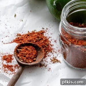 A small glass jar filled with vibrant homemade Chili Lime Seasoning (Tajin) is prominently displayed on a simple white surface. The seasoning's rich color and fine texture are showcased, inviting viewers to experience its zesty and spicy flavors. The jar is sealed, implying freshness and readiness for use.
