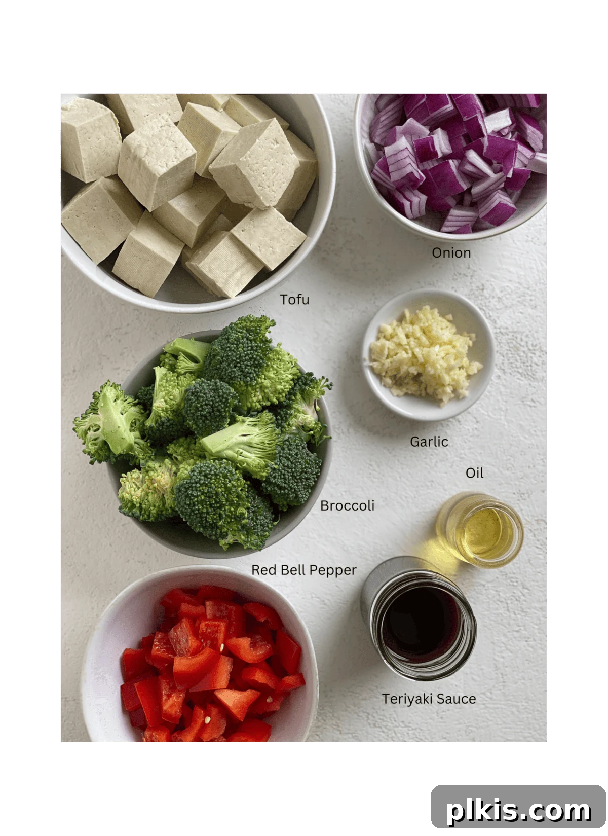 Speedy Teriyaki Tofu Bowl 3 Ingredients for Quick Teriyaki Tofu Stir Fry measured out against a white surface, including tofu, bell peppers, onion, broccoli, garlic, and teriyaki sauce
