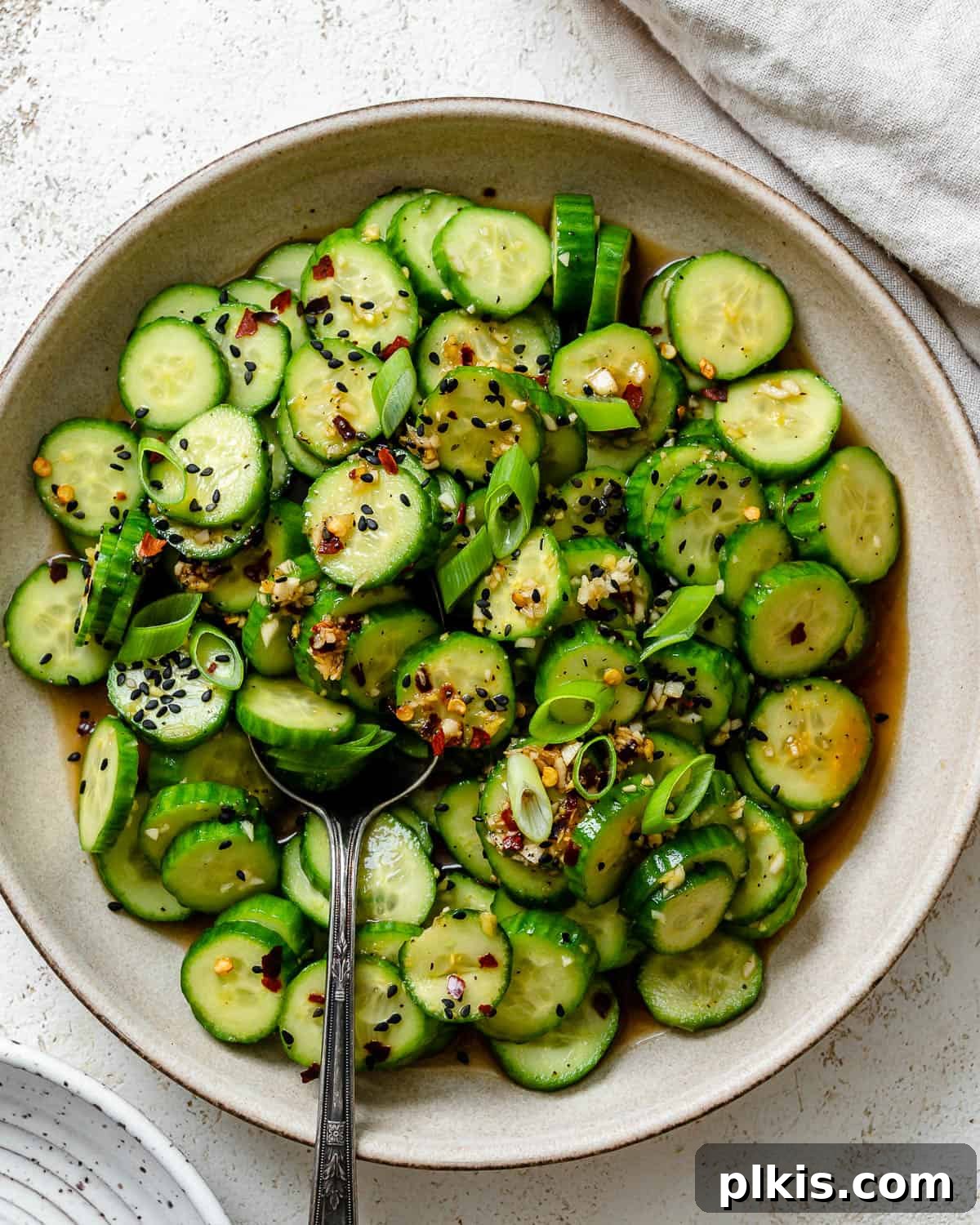 Sassy Cucumber Slaw 2 Completed Spicy Asian Cucumber Salad plated on a white plate against a white background, garnished with sesame seeds and green onions.