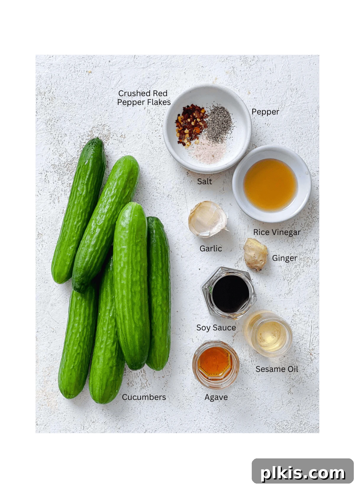 Sassy Cucumber Slaw 3 Ingredients for Spicy Asian Cucumber Salad measured out against a white surface, including sliced cucumbers, soy sauce, rice vinegar, sesame oil, garlic, ginger, and red pepper flakes.
