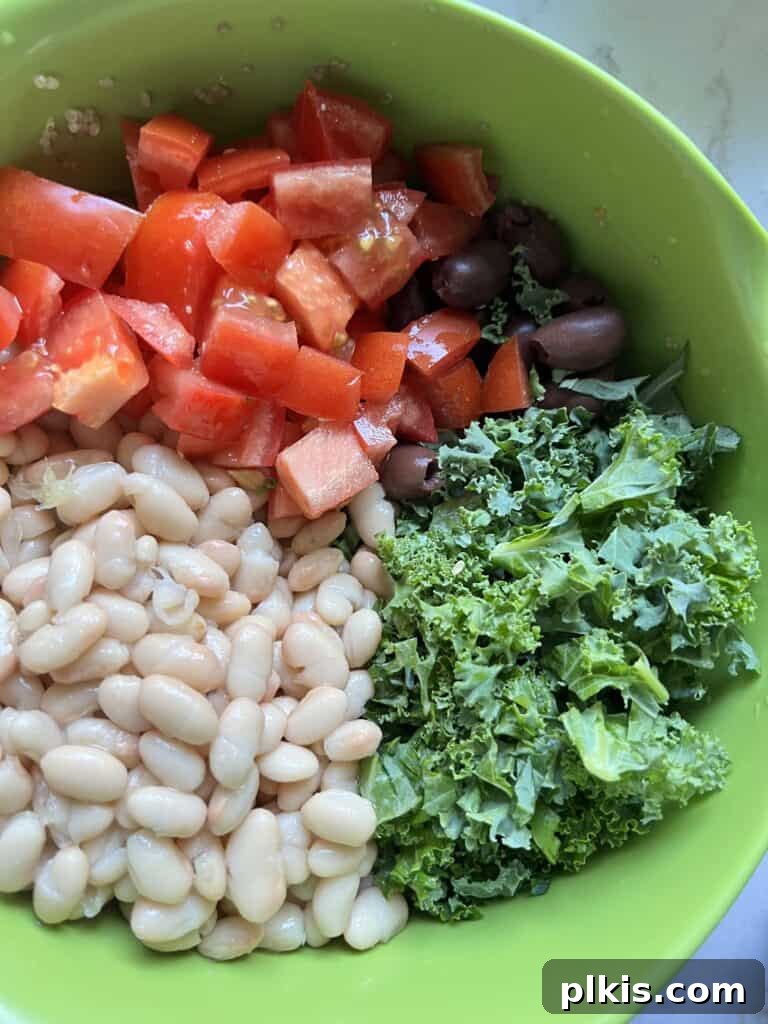 Zesty Mediterranean Vegan Quinoa 4 Process shot showing a vibrant mix of chopped vegetables, including kale, tomatoes, and olives, in a green mixing bowl, ready for the quinoa.