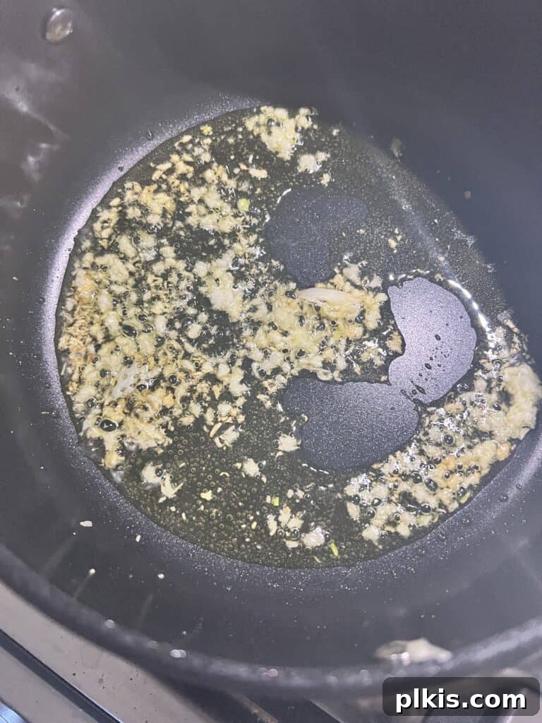 Zesty Mediterranean Vegan Quinoa 6 Process shot showing minced garlic sizzling in olive oil in a small saucepan, creating the aromatic base for the dressing.