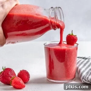 process of pouring completed strawberry juice from a jar into a cup with scattered strawberries against a white background