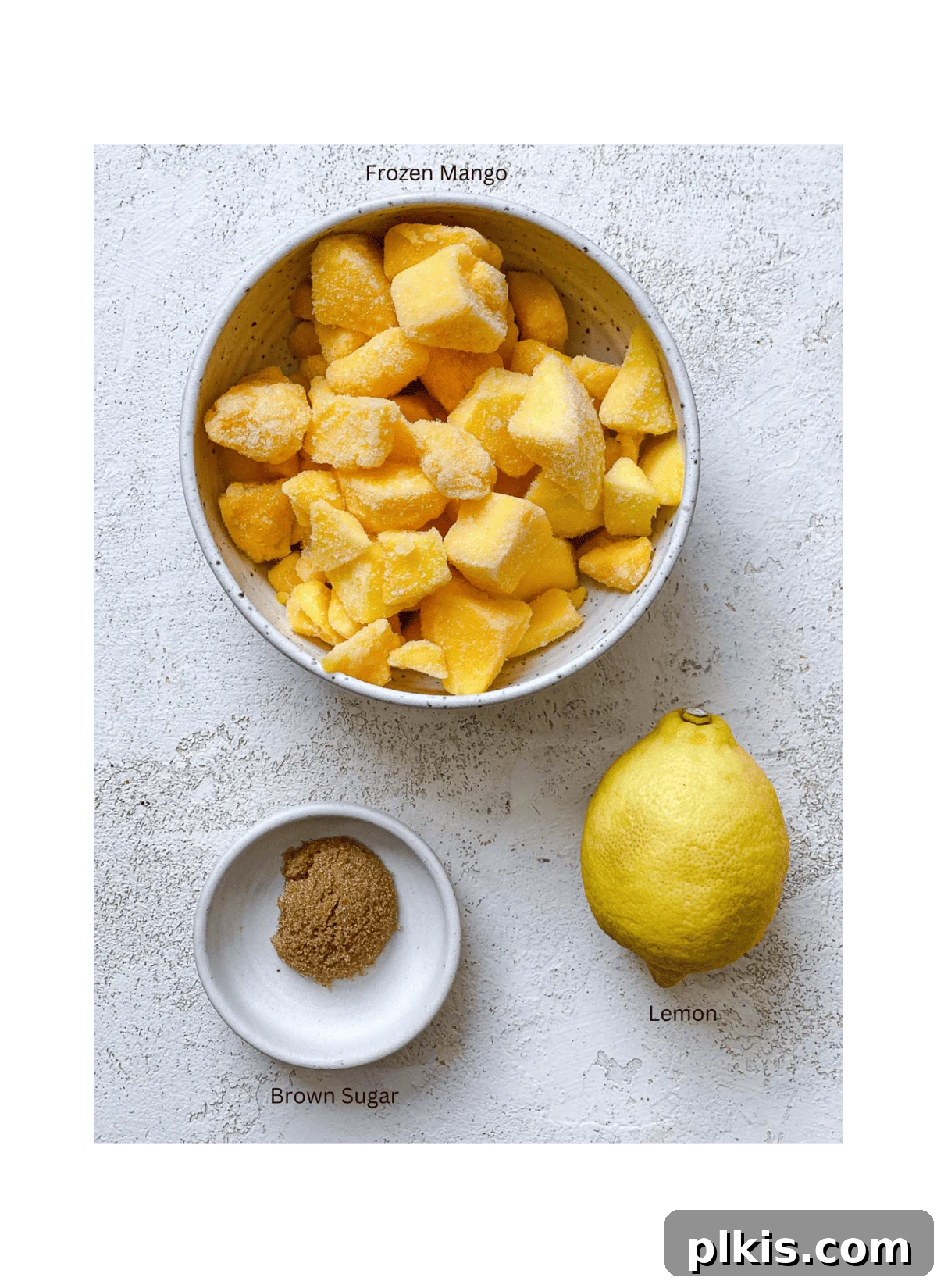 Versatile 3-Ingredient Mango Topping 3 A simple arrangement of fresh mango chunks, granulated sugar, and a lime, representing the three core ingredients for mango compote, laid out on a clean white surface.