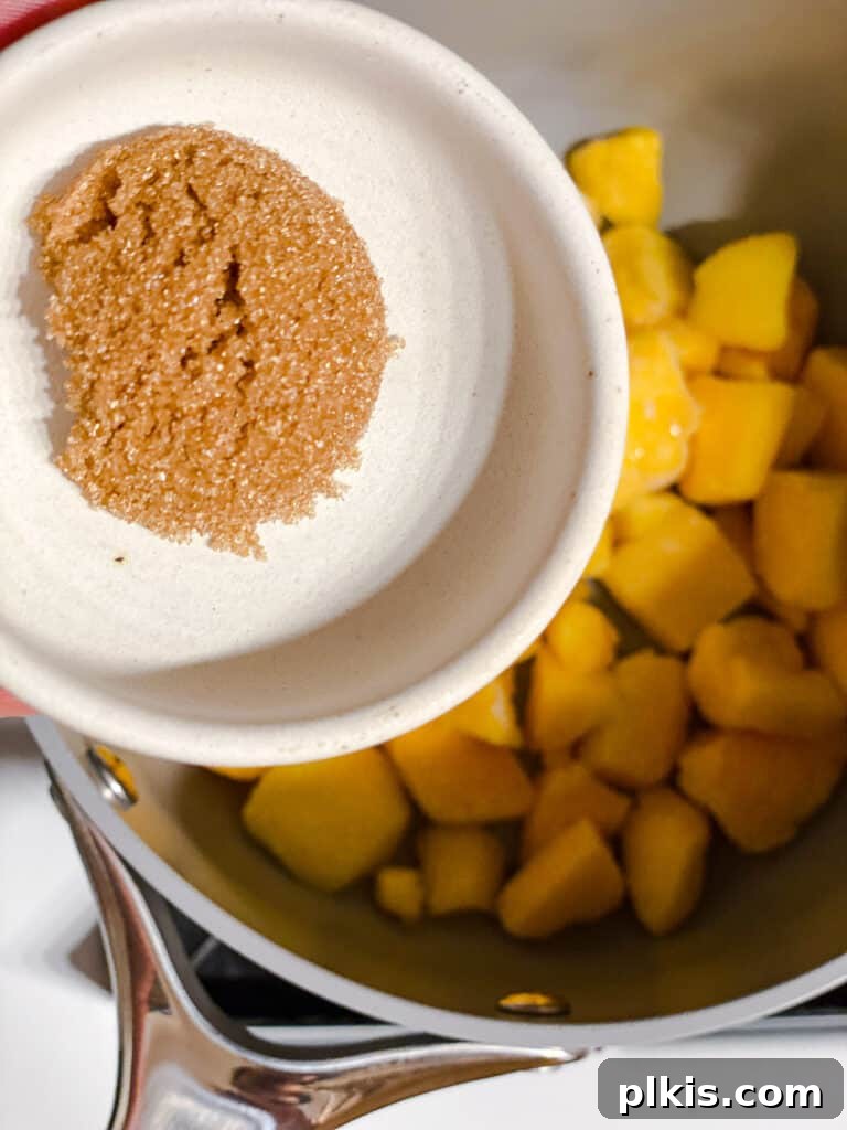 Versatile 3-Ingredient Mango Topping 5 Brown sugar being carefully added to a pot of mango chunks, illustrating the sweetening step of the compote recipe.