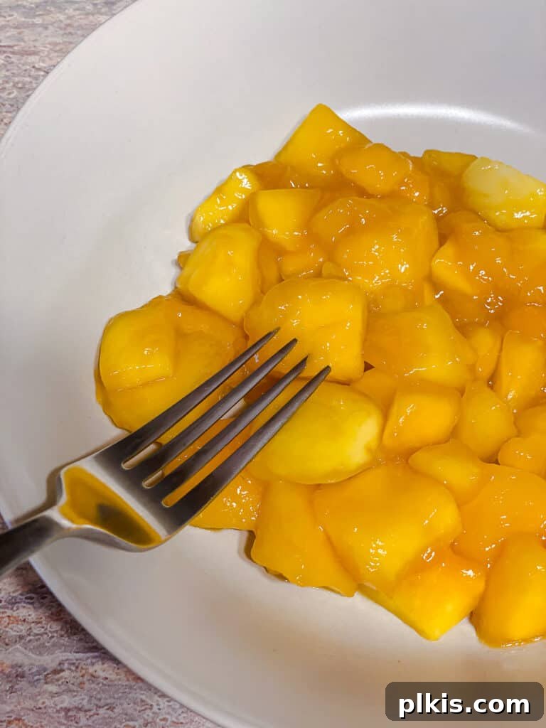 Versatile 3-Ingredient Mango Topping 8 A hand gently mashing softened mango chunks in a pot with a potato masher, demonstrating how to create a chunky compote texture.