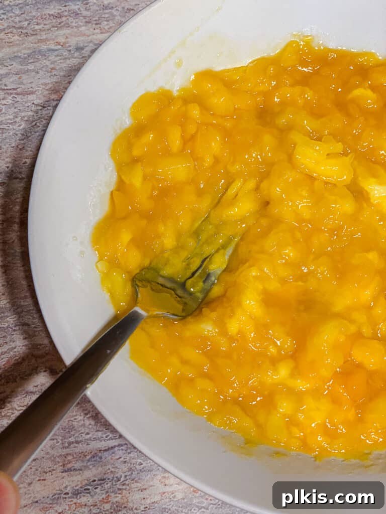 Versatile 3-Ingredient Mango Topping 9 Close-up shot of hand mashing mangos in a pot, showcasing the evolving chunky texture of the compote as it cooks.