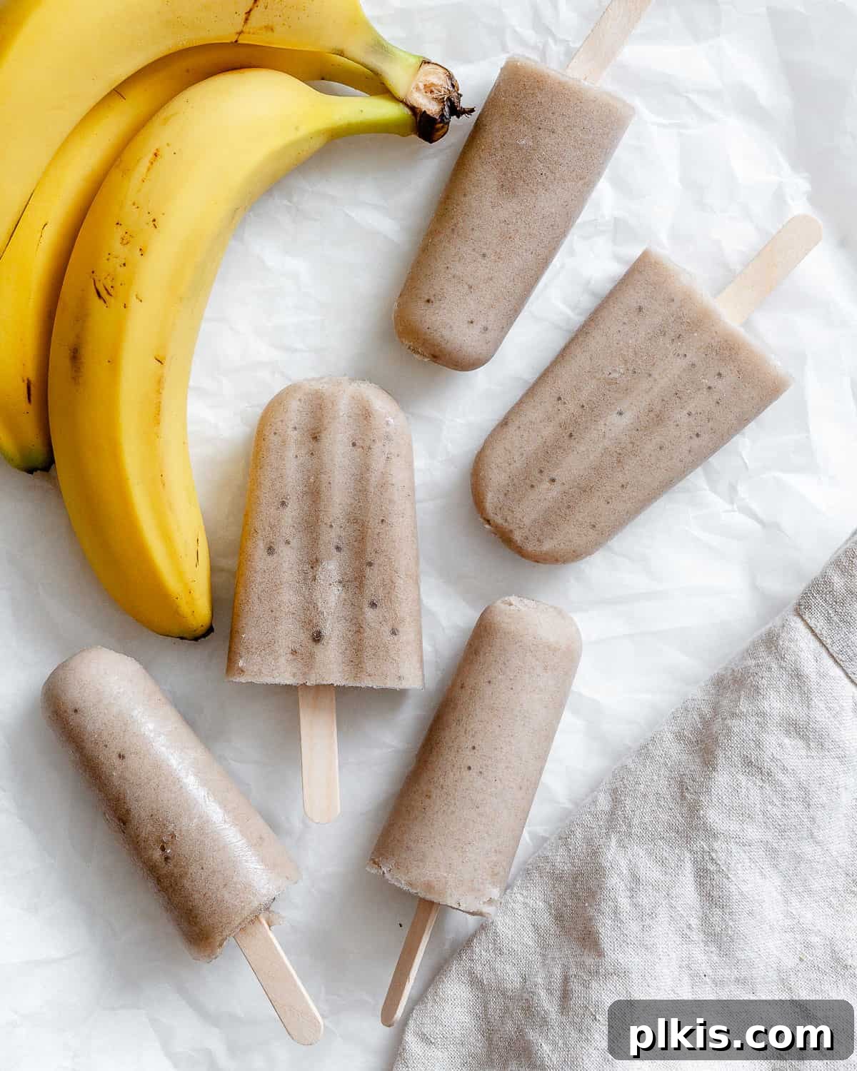 Naturally Sweet Banana Pops 2 Delicious and healthy banana popsicles displayed on a white surface next to fresh bananas, showcasing a perfect summer treat.