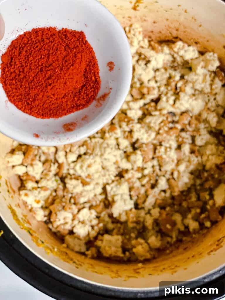 Hearty Vegan Ragu 12 Process shot of smoked paprika and other spices being added to the browned tofu in the pot, stirring to combine.