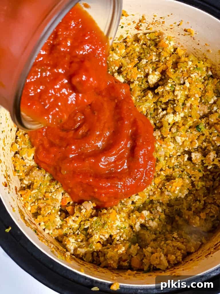 Hearty Vegan Ragu 13 Process shot of marinara sauce being poured into the pot with the browned tofu and cooked vegetables.