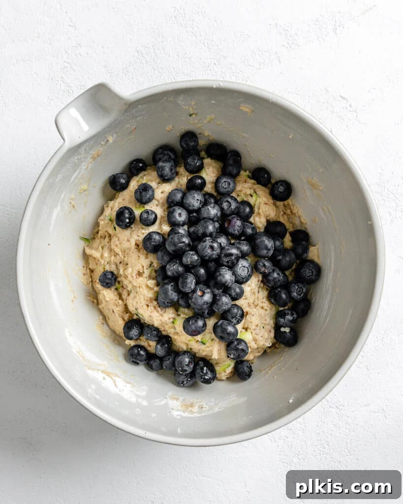 Garden-Fresh Vegan Blueberry Zucchini Muffins 6 Process of adding blueberries to batter against white background.