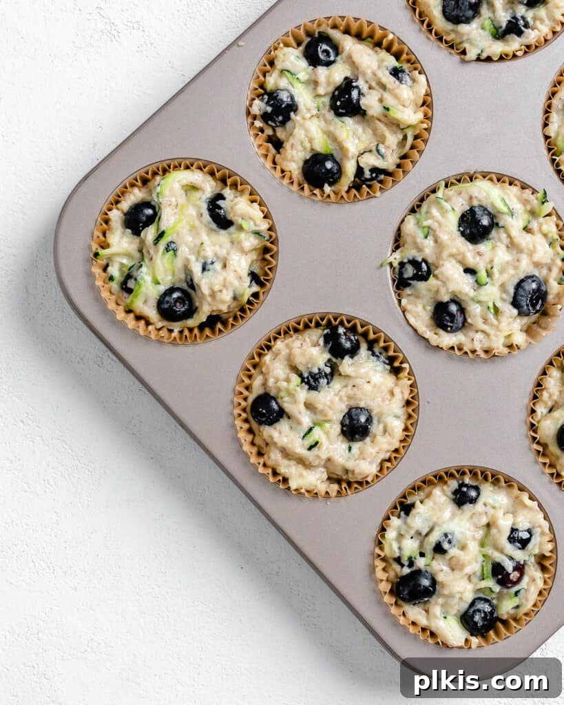 Garden-Fresh Vegan Blueberry Zucchini Muffins 7 Process of adding batter and blueberries to the top of batter in a muffin tin against a white background.