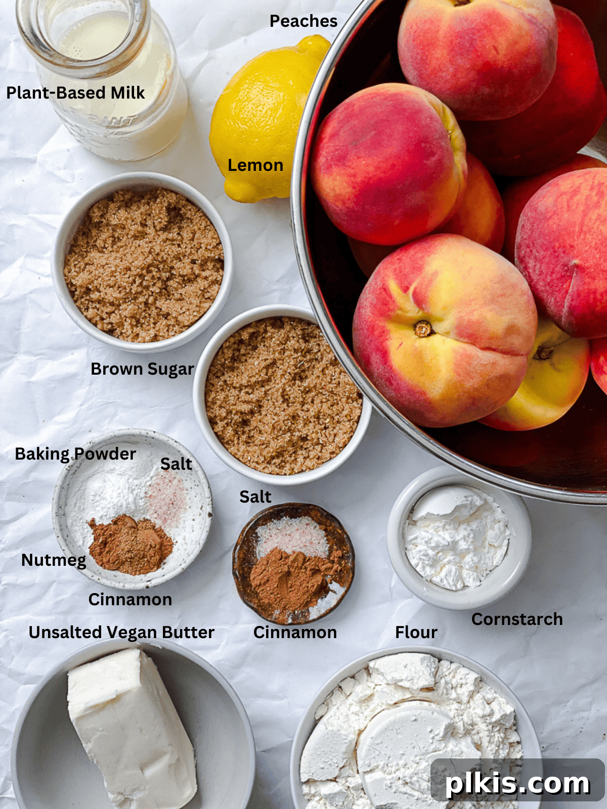 Effortless Vegan Peach Cobbler 3 Various ingredients for Easy Vegan Peach Cobbler laid out on a white surface, including peaches, flour, sugar, and spices.