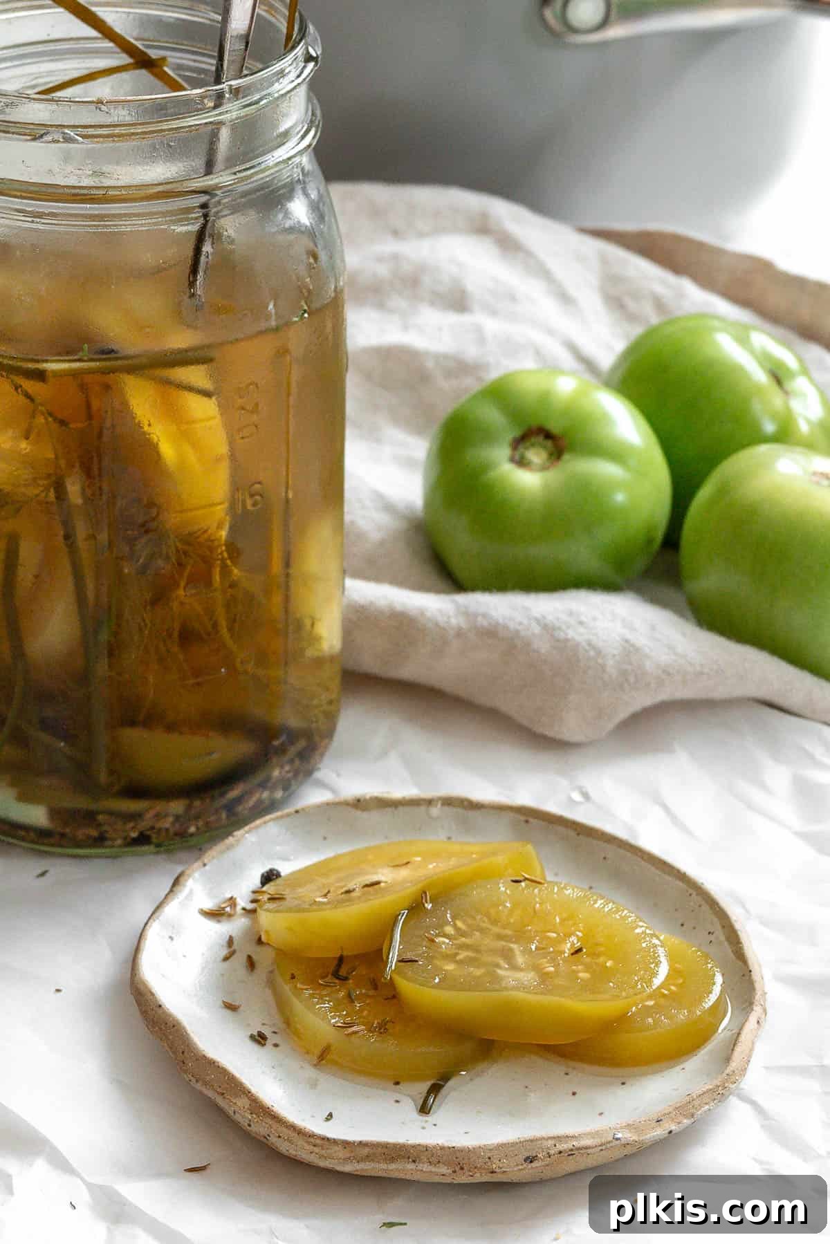 Tangy Green Tomatoes in a Flash 2 A vibrant plate of quick pickled green tomatoes, served alongside a glass jar filled with more pickled tomatoes and a scattering of fresh, raw green tomatoes.