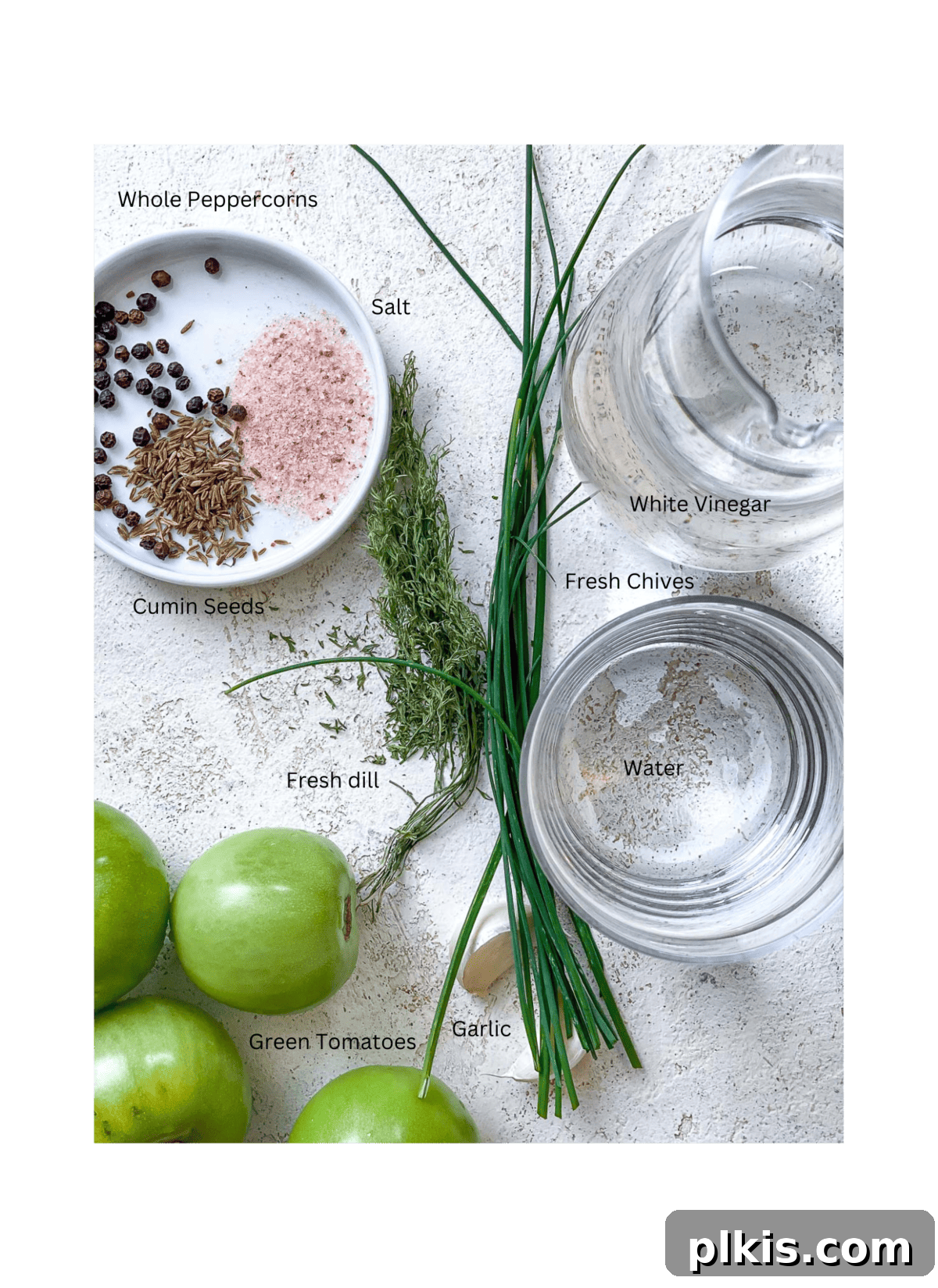 Tangy Green Tomatoes in a Flash 3 Precisely measured ingredients for quick pickled green tomatoes, including sliced green tomatoes, vinegar, water, salt, garlic, dill, chives, cumin seeds, and peppercorns, arranged on a clean white surface.