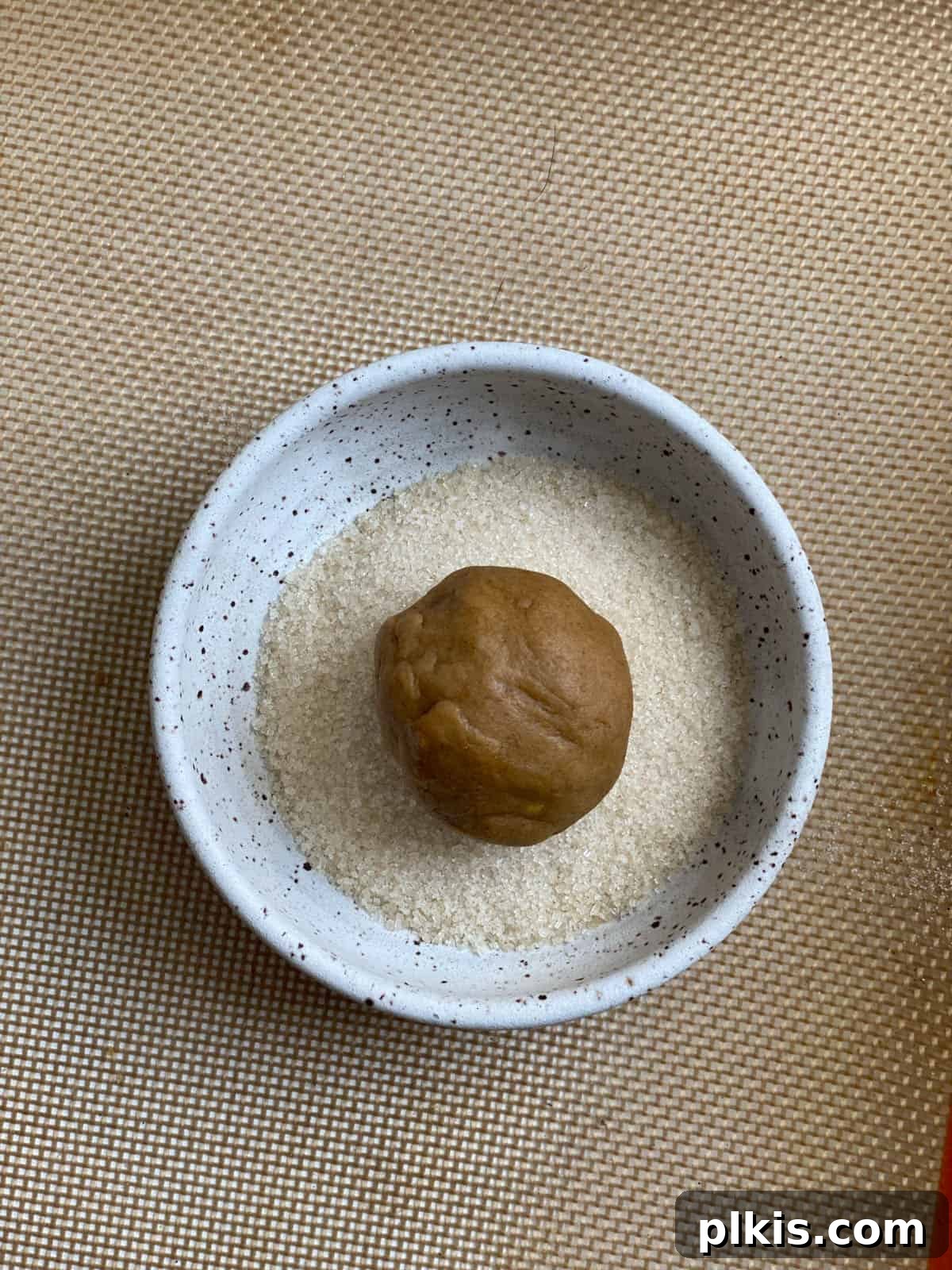 Bold Triple Ginger Vegan Snaps 13 Close-up of a cookie dough ball being rolled in granulated sugar within a small bowl.