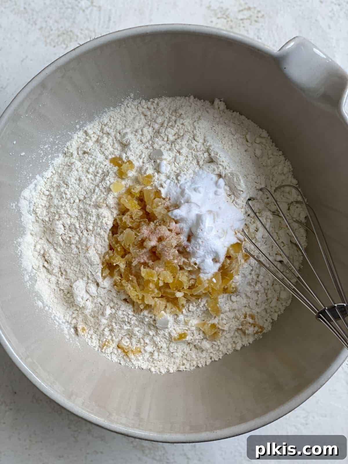 Bold Triple Ginger Vegan Snaps 5 Process shot showing dry ingredients (flour, baking soda, salt, minced crystallized ginger) being mixed in a bowl with a whisk.