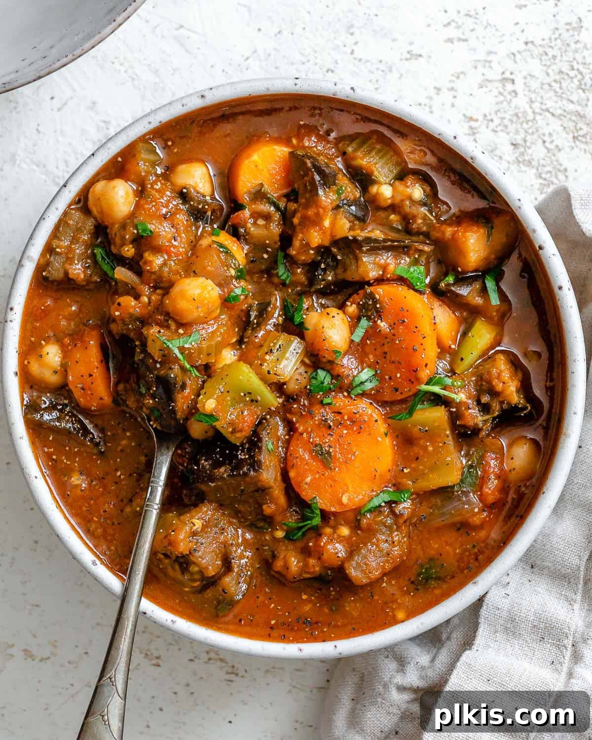 Hearty Eggplant, Tomato, and Chickpea Stew 2 Rich and flavorful Eggplant Stew with Tomatoes and Chickpeas, garnished with fresh herbs, served in a rustic bowl on a white surface.