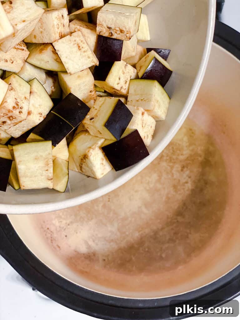 Hearty Eggplant, Tomato, and Chickpea Stew 6 Eggplant cubes being added to a hot pot with oil.