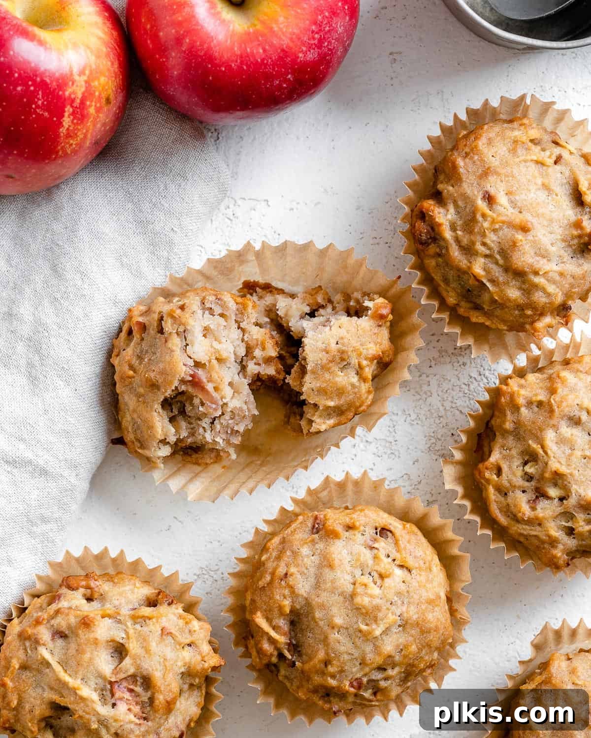 Wholesome Vegan Apple Muffins 2 Several completed Vegan Apple Muffins spread out on a white surface, showcasing their golden-brown tops and moist texture.