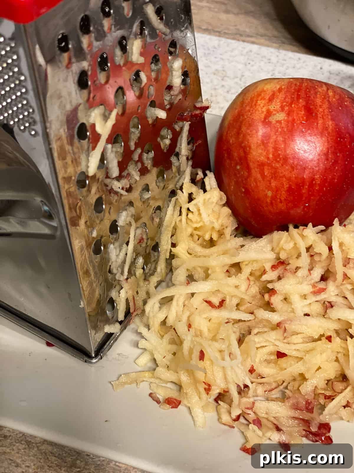 Wholesome Vegan Apple Muffins 4 Process shot of grating apples with a whole apple in the background, showing freshly grated apple.
