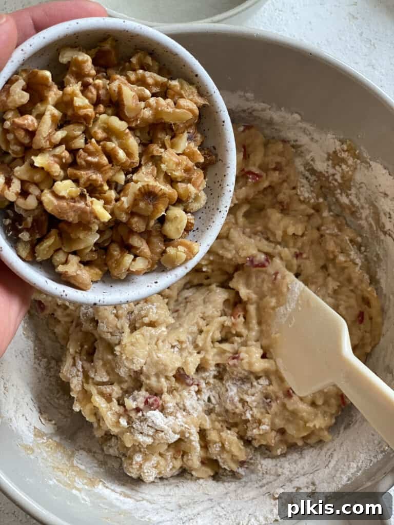 Wholesome Vegan Apple Muffins 8 Process of adding chopped walnuts to the apple muffin mixture, illustrating optional add-ins.