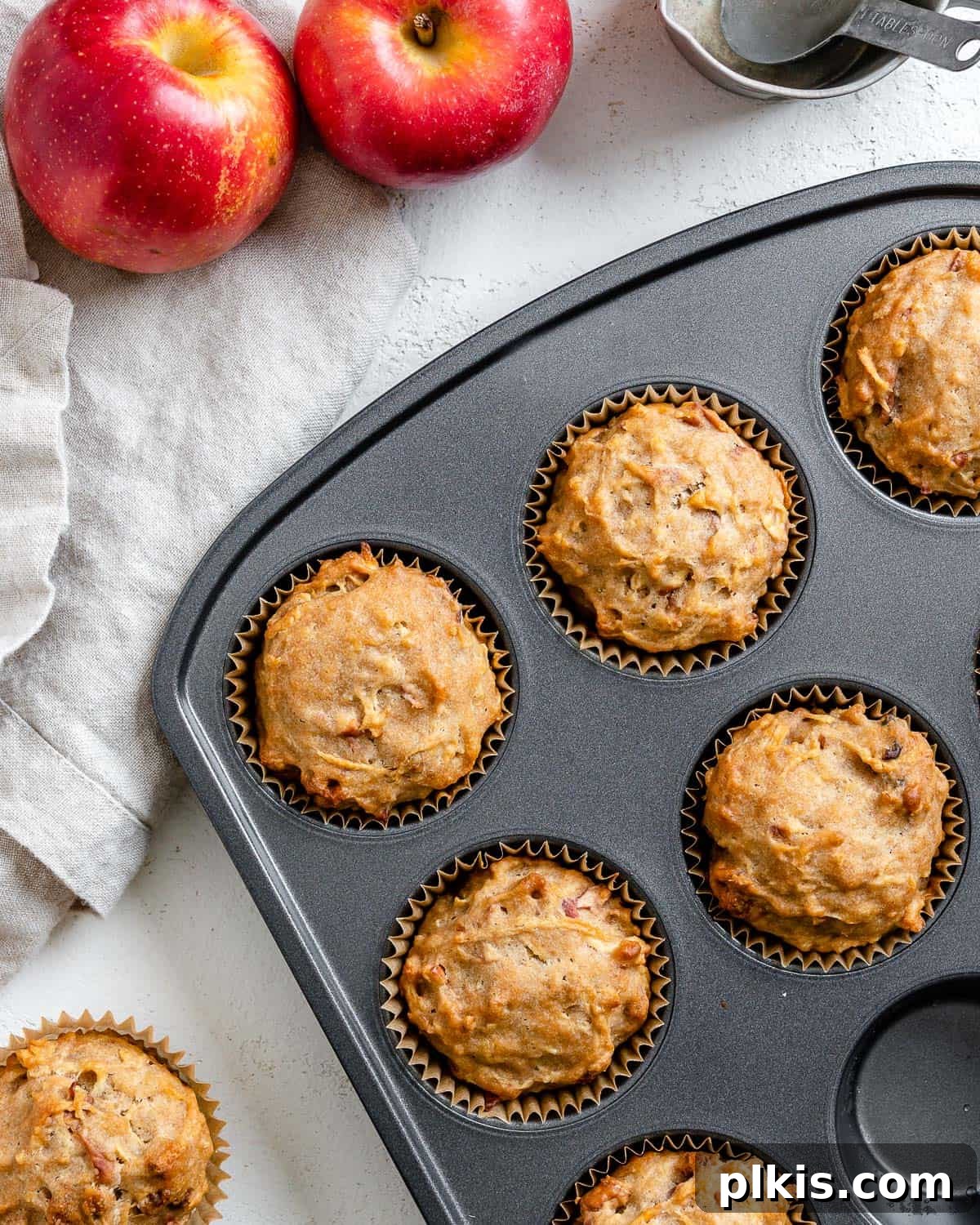 Wholesome Vegan Apple Muffins 10 Several completed Vegan Apple Muffins spread out on a white surface, showcasing their golden-brown tops and moist texture.