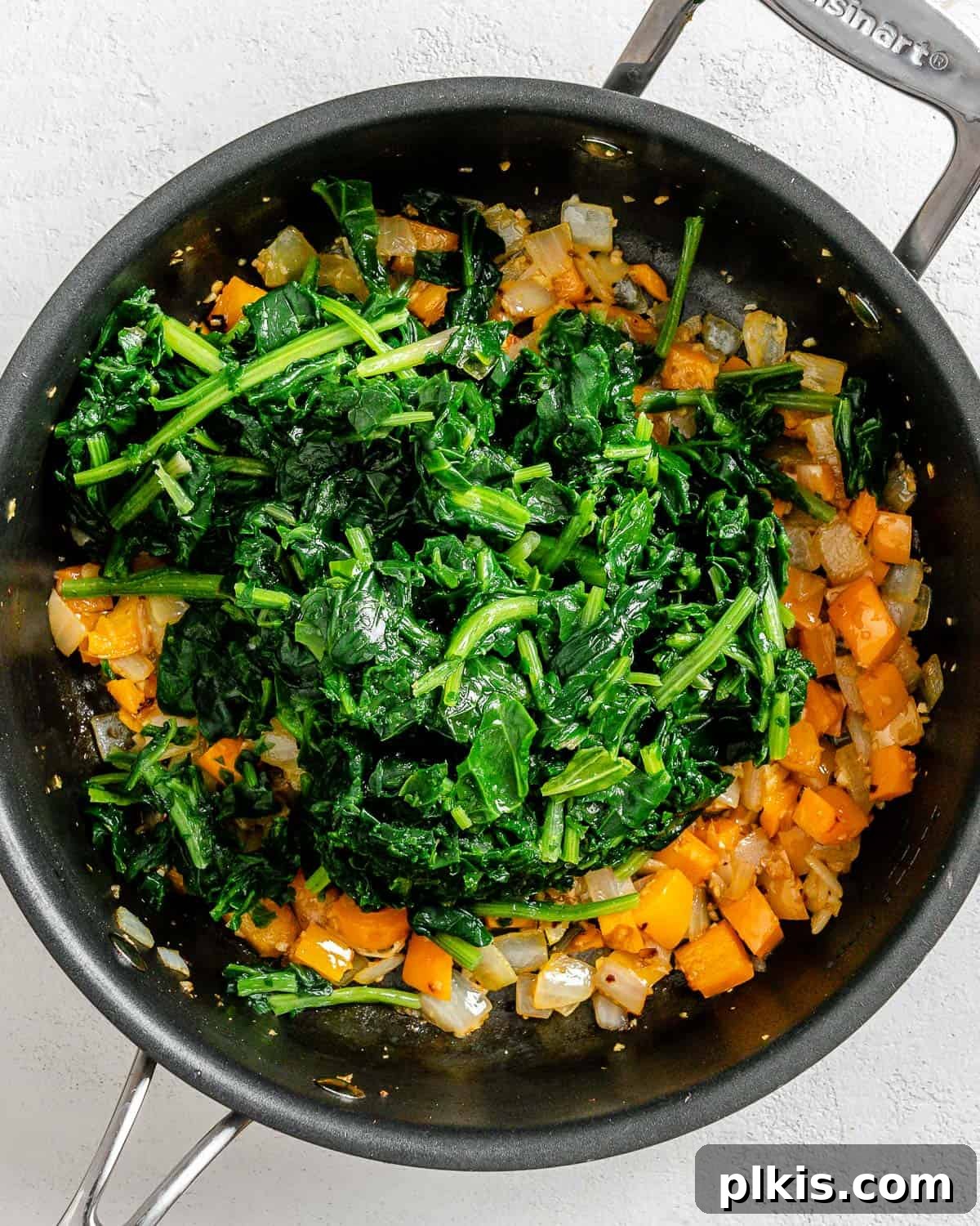 Golden Polenta Spinach Bake 11 A process shot of mixing thawed spinach into the sautéed vegetables in a black pan, ensuring even distribution.