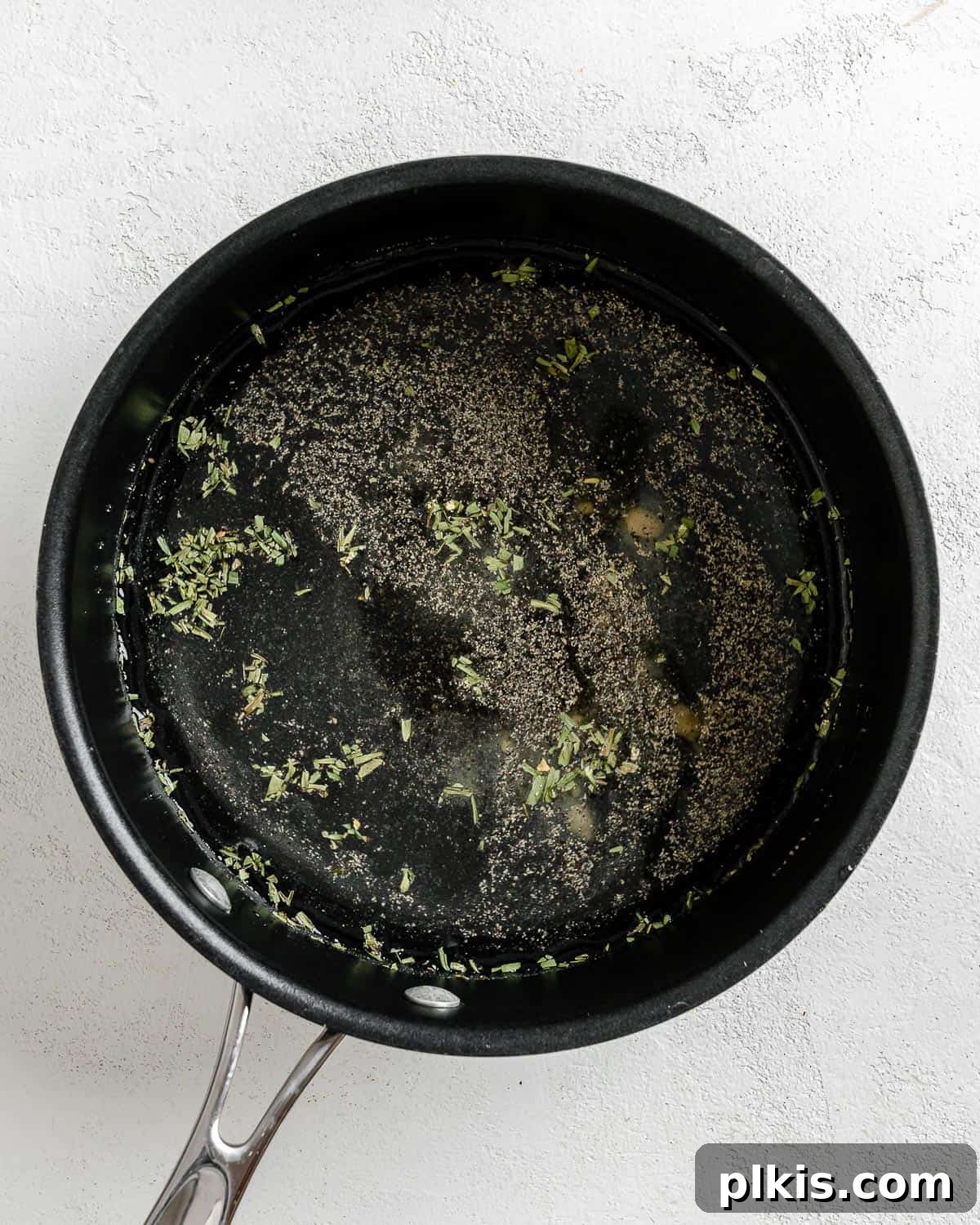 Golden Polenta Spinach Bake 13 A process shot of mixing water with salt, tarragon, mustard powder, and black pepper in a black saucepan to prepare the polenta liquid.