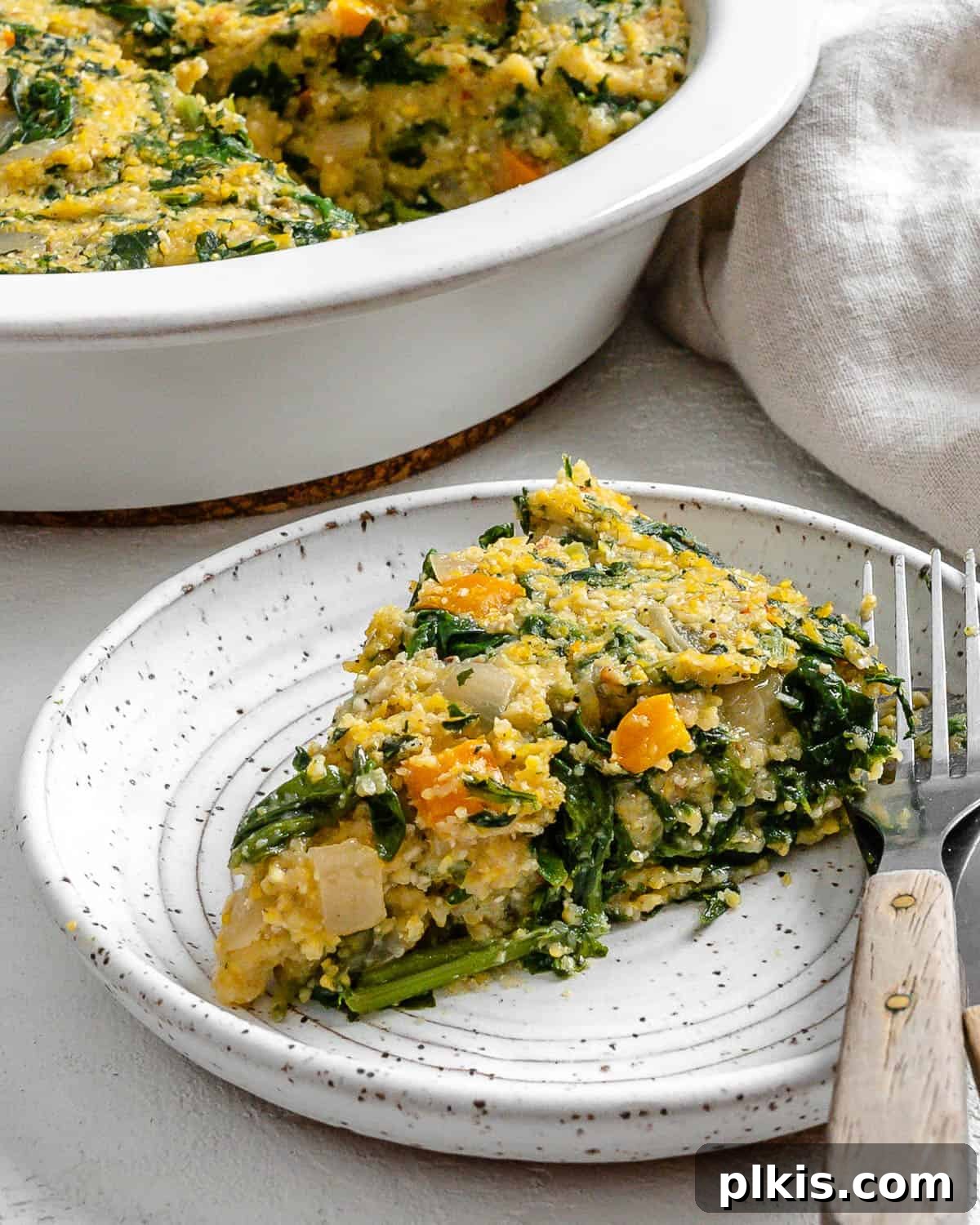 Golden Polenta Spinach Bake 19 A perfectly sliced piece of Garlicky Spinach and Pepper Polenta Pie on a white speckled plate, with the rest of the pie visible in a container in the background.