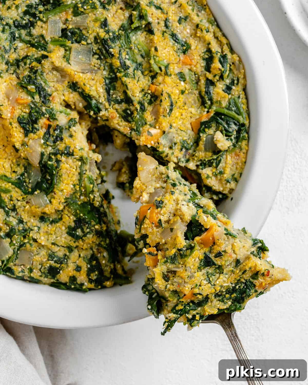 Golden Polenta Spinach Bake 20 A golden-brown slice of Garlicky Spinach and Pepper Polenta Pie being gently pulled from the whole pie, showcasing its vibrant filling of spinach and orange peppers.