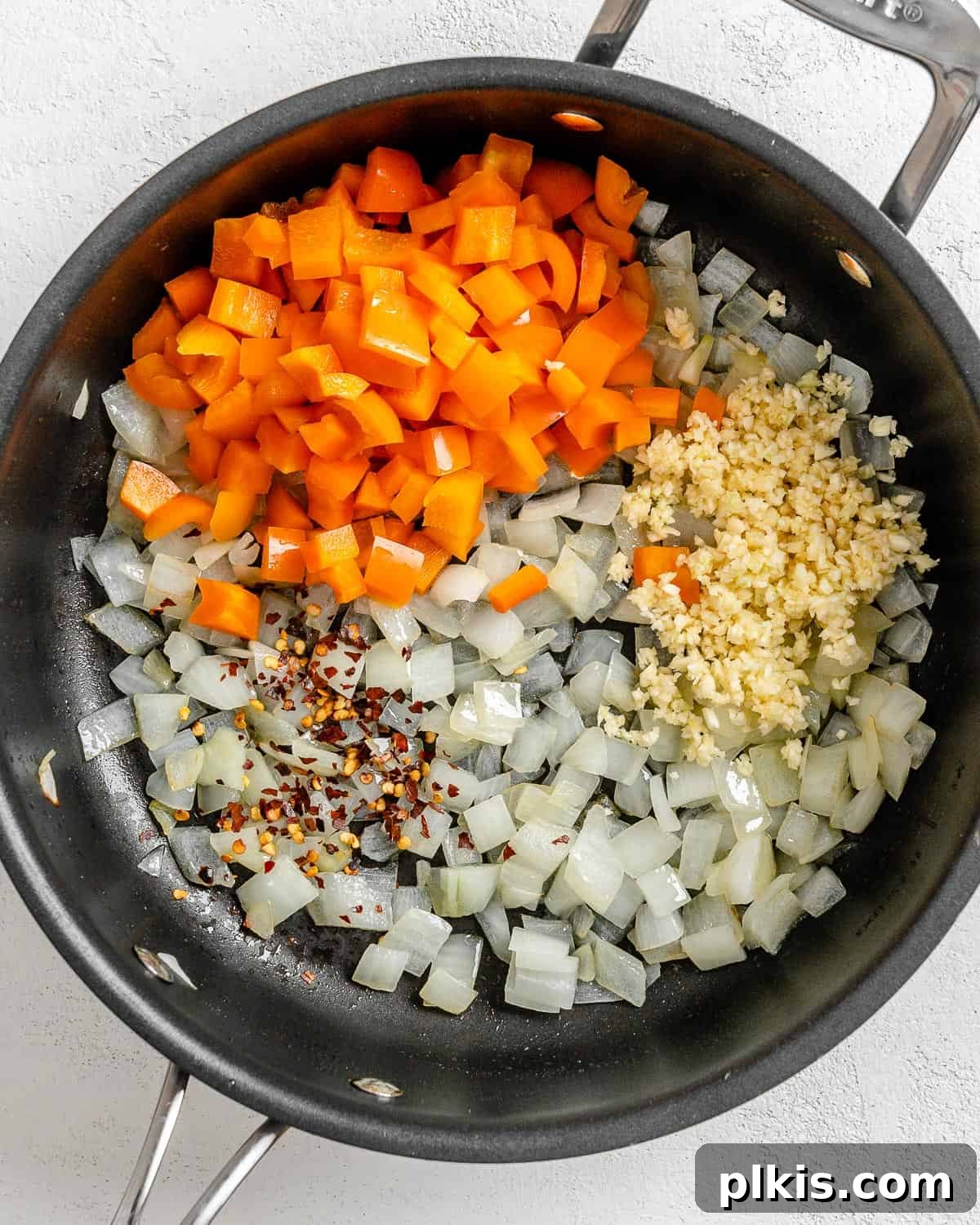 Golden Polenta Spinach Bake 9 A process shot showing the addition of diced orange bell pepper, red pepper flakes, and minced garlic to the sautéed onions in a black pan.
