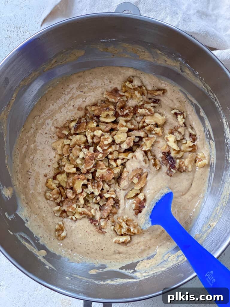 Moist Coffee Walnut Loaf 6 A process shot demonstrating walnuts being gently folded into the prepared vegan coffee loaf cake batter in a mixing bowl.