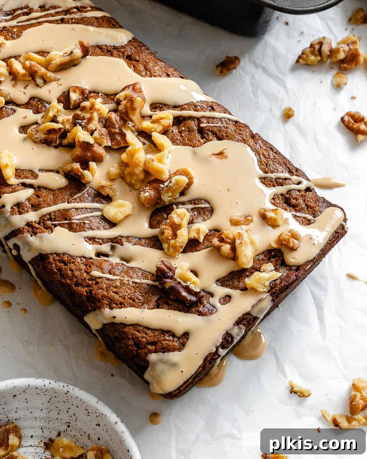 Moist Coffee Walnut Loaf 8 A perfectly glazed vegan coffee and walnut loaf cake, garnished with extra walnuts, resting on a white surface, ready to be sliced.