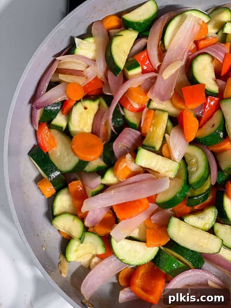 Speedy Zucchini Stir-Fry 7 A mix of colorful stir-fry vegetables, including zucchini, carrots, and bell peppers, cooking in a pan.