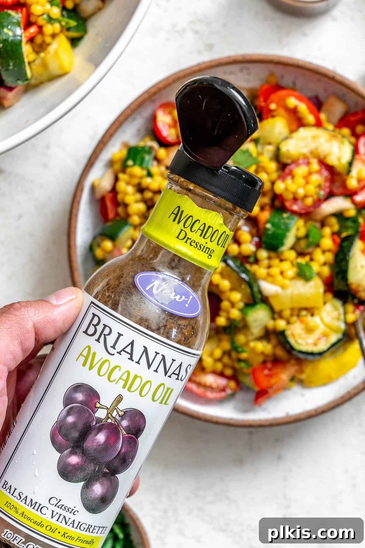 Vibrant Garden Couscous Salad 17 Close-up of balsamic vinaigrette bottle with the finished Couscous Salad with Roasted Vegetables in the background.