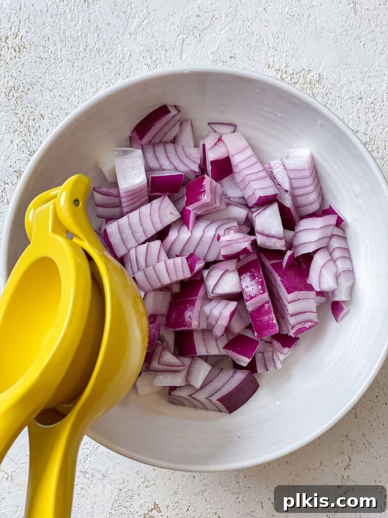 Vibrant Garden Couscous Salad 7 Process shot of squeezing fresh lemon juice over sliced red onions in a bowl.