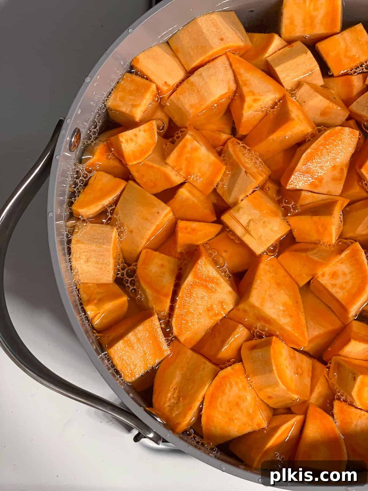 Velvety Vegan Sweet Potato Mash 5 A large pot filled with chopped and peeled sweet potatoes submerged in boiling water on a stove.