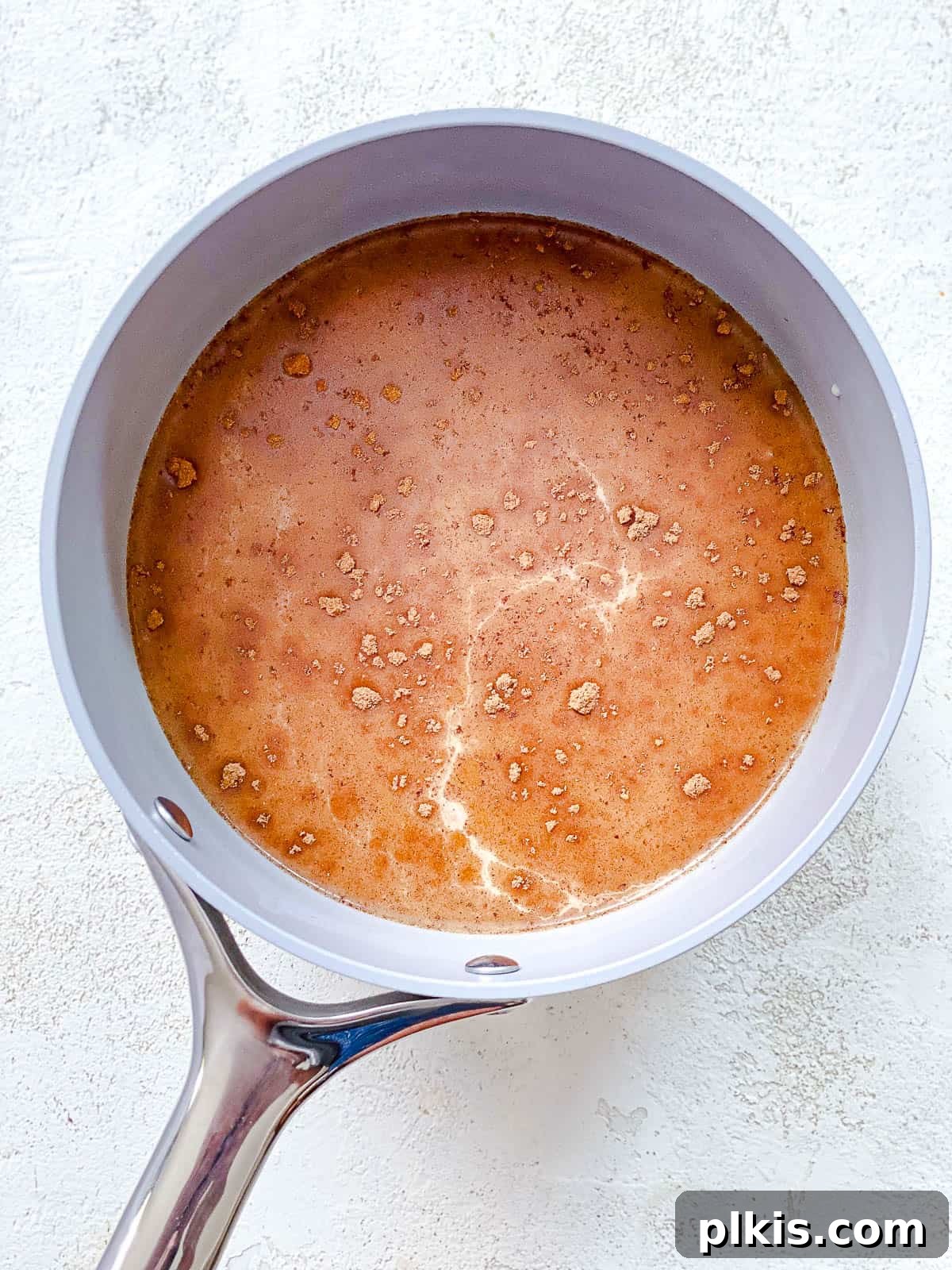 The Ultimate Plant-Based Pumpkin Spice Latte 6 A gray pot containing milk, pumpkin puree, and pumpkin pie spice, all mixed together on a textured white surface, showing the blend of ingredients before the final touches.