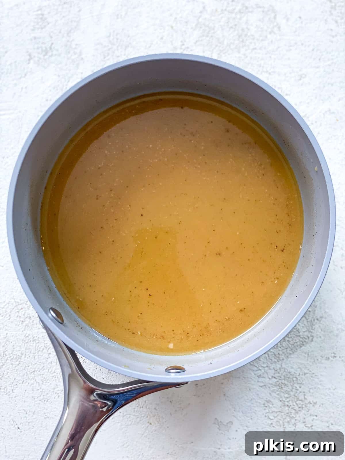 The Ultimate Plant-Based Pumpkin Spice Latte 7 A gray pot filled with the fully mixed vegan pumpkin spice latte base, featuring milk, pumpkin puree, vanilla, sweetener, and pumpkin pie spice, on a textured white surface, ready to be served.