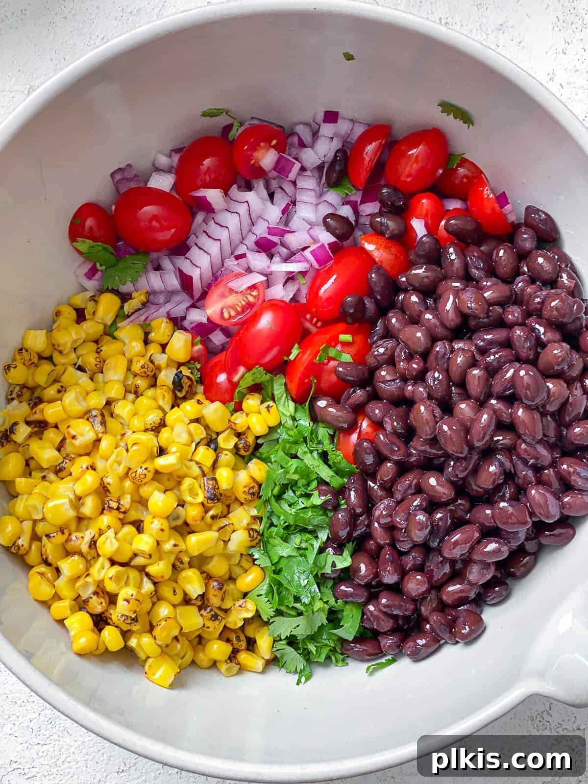 Vegan Fiesta Bowl 7 A large white bowl brimming with a colorful mixture of roasted corn, fresh chopped cilantro, plump black beans, juicy halved cherry tomatoes, and finely diced red onions.