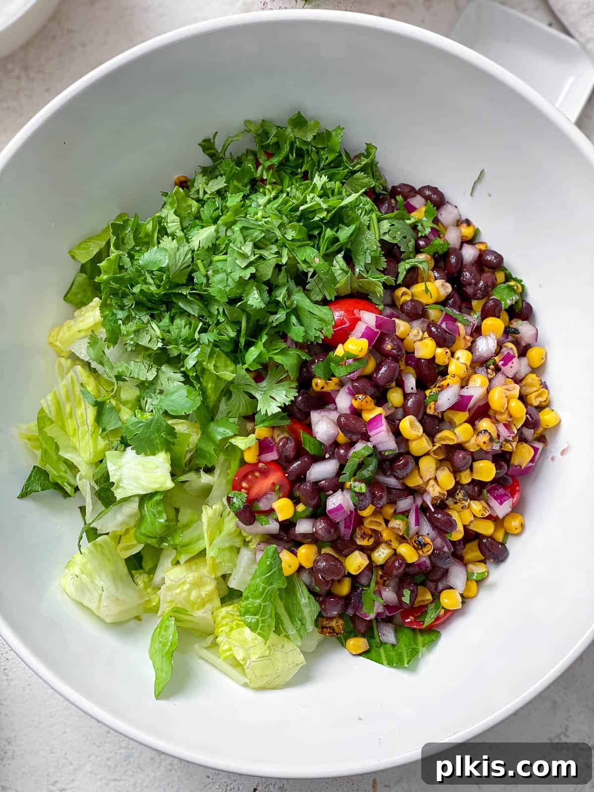 Vegan Fiesta Bowl 8 A generously sized white bowl filled with a fresh and vibrant vegan taco salad, featuring crisp chopped romaine lettuce, sweet roasted corn, aromatic chopped cilantro, hearty black beans, juicy halved cherry tomatoes, and finely diced onions, all beautifully combined.