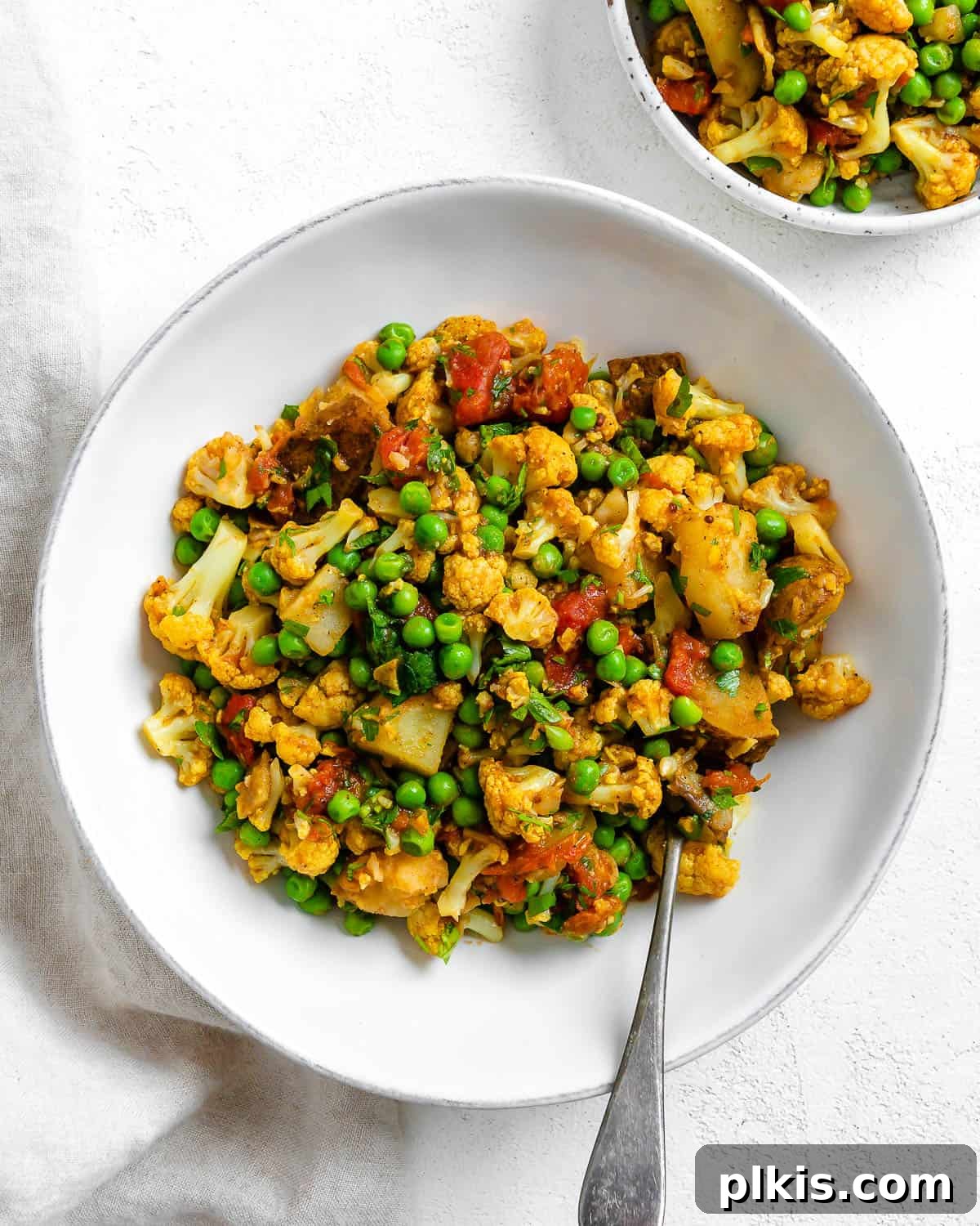 30 Effortless Plant-Based Potato Creations 13 complete Aloo Gobi (Curried Potatoes, Cauliflower, and Peas) in a white bowl