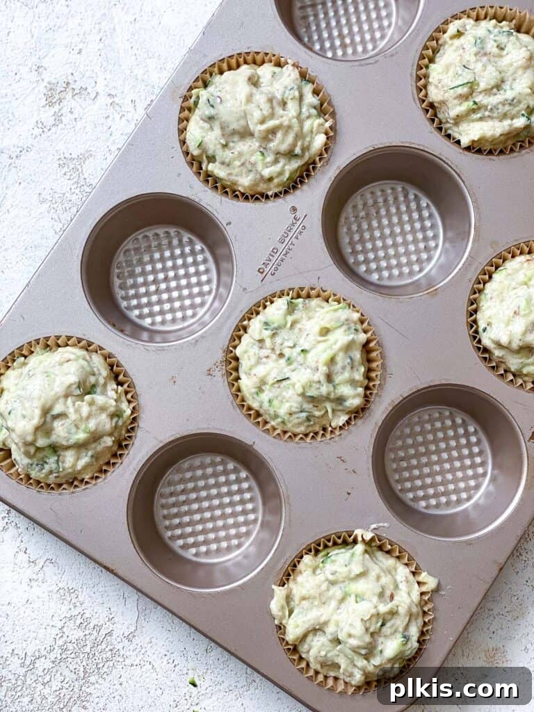 Wholesome Vegan Zucchini Muffins 8 A process shot showing the muffin batter being carefully added to a lined muffin tin, ready for baking.
